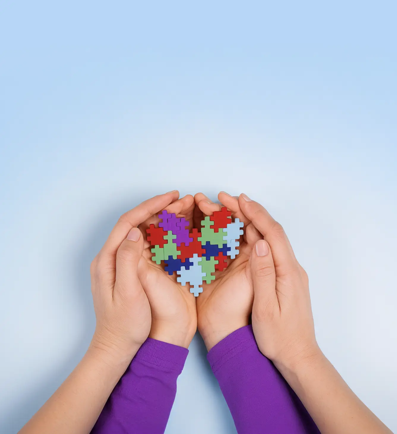 Child's hands and adult hands holding a colorful puzzle piece heart representing autism support and ABA therapy at CAI ABA in Hurst TX